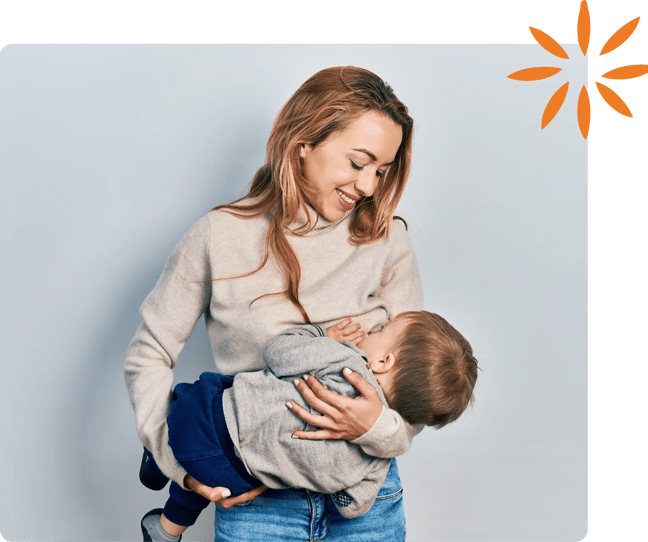 Mother breastfeeding her toddler while holding him in her arms and smiling.