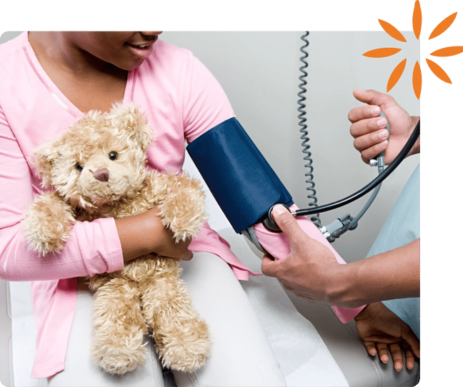 Child holding a teddy bear while having blood pressure checked.